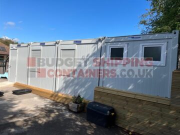 External side view of modular building install, showing smart grey modular units, with window shutters closed, and customer has added some wooden cladding to improve looks.