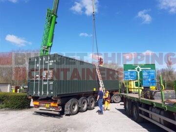 Green shipping container being lifted by a crane from flatbed truck