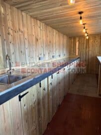 Contianer bar internal view showing rear sideboard, sink and cupboards set against a cladded rear wall.