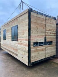cladded shipping container with windows being lowered to the ground with chains