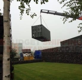 Crane equipped truck lifting a shipping container over a fence